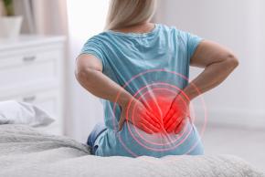 photo d'une femme en tshirt bleue, assise, les mains dans le dos, avec un point rouge dans le dos symbolisant la douleur