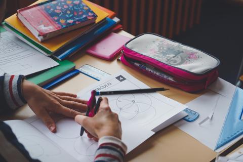 photo représentant les mains d'un enfant travaillant sur sa table, avec cahier, crayon et trousse
